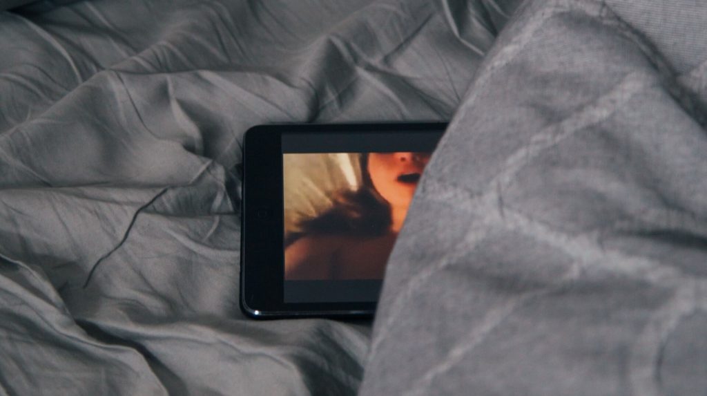 An image of a partially covered cell phone on a bed with a woman on the screen
